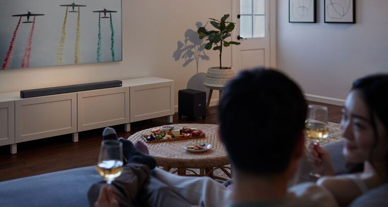 a couple watching TV with a large sound bar sitting under it. a couple watching TV with a large sound bar sitting under it.